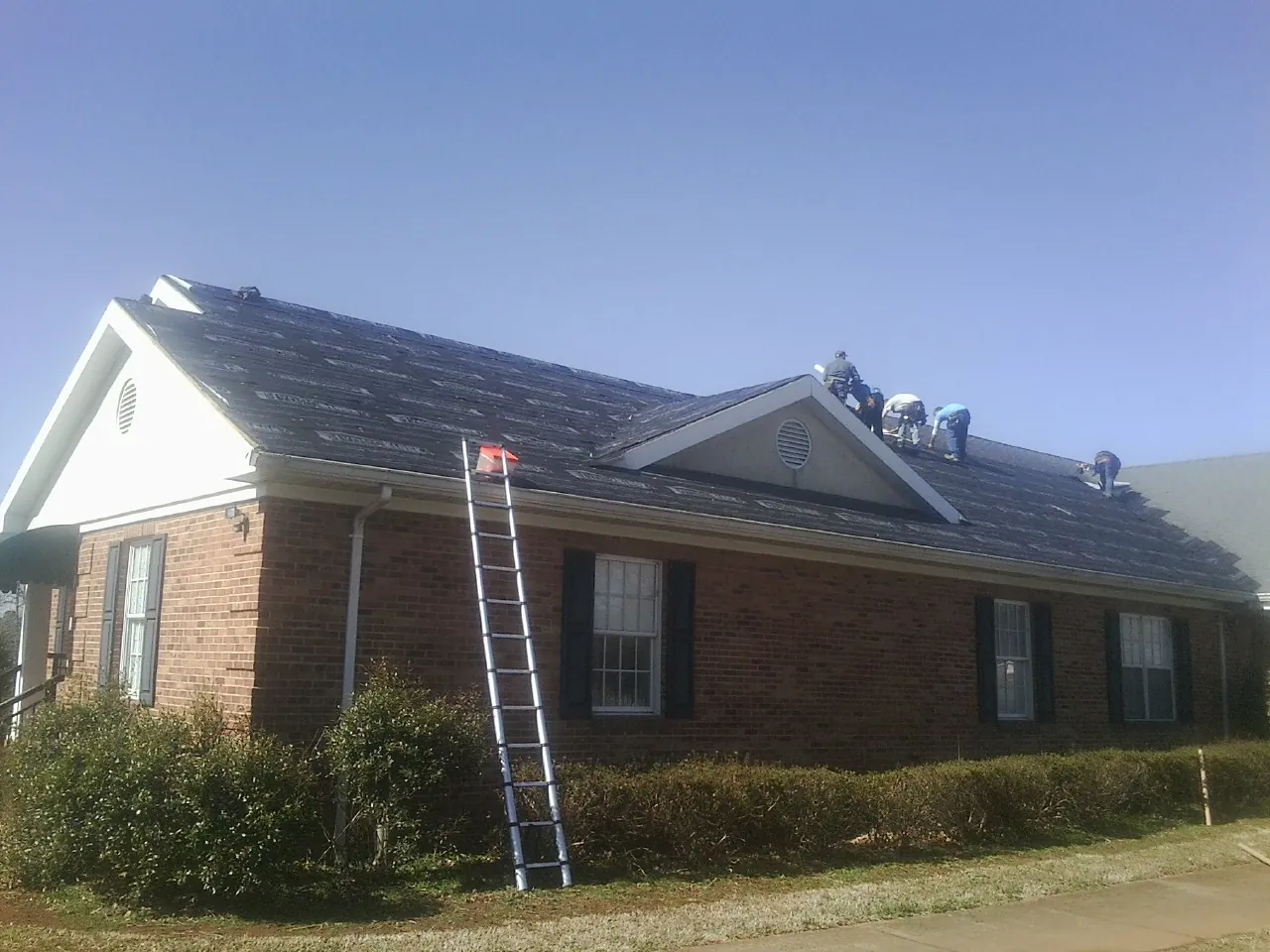 Crew tearing shingles off a brick ranch roof with a ladder set — Metal Roof Repair work by our crew in La Habra