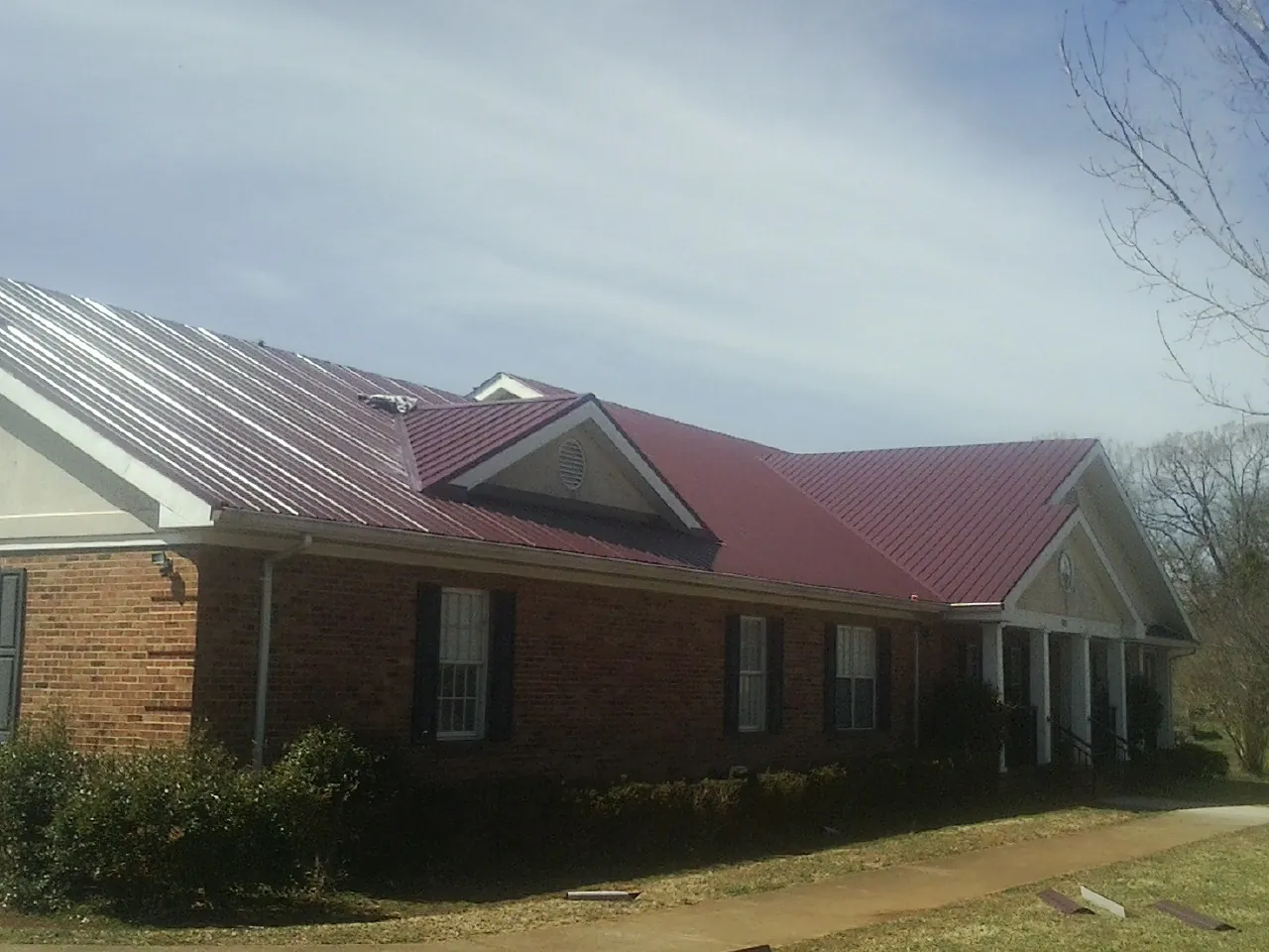 Red metal roof with gabled entries on a long brick building, from a Hail Damage Roof Repair job in La Habra