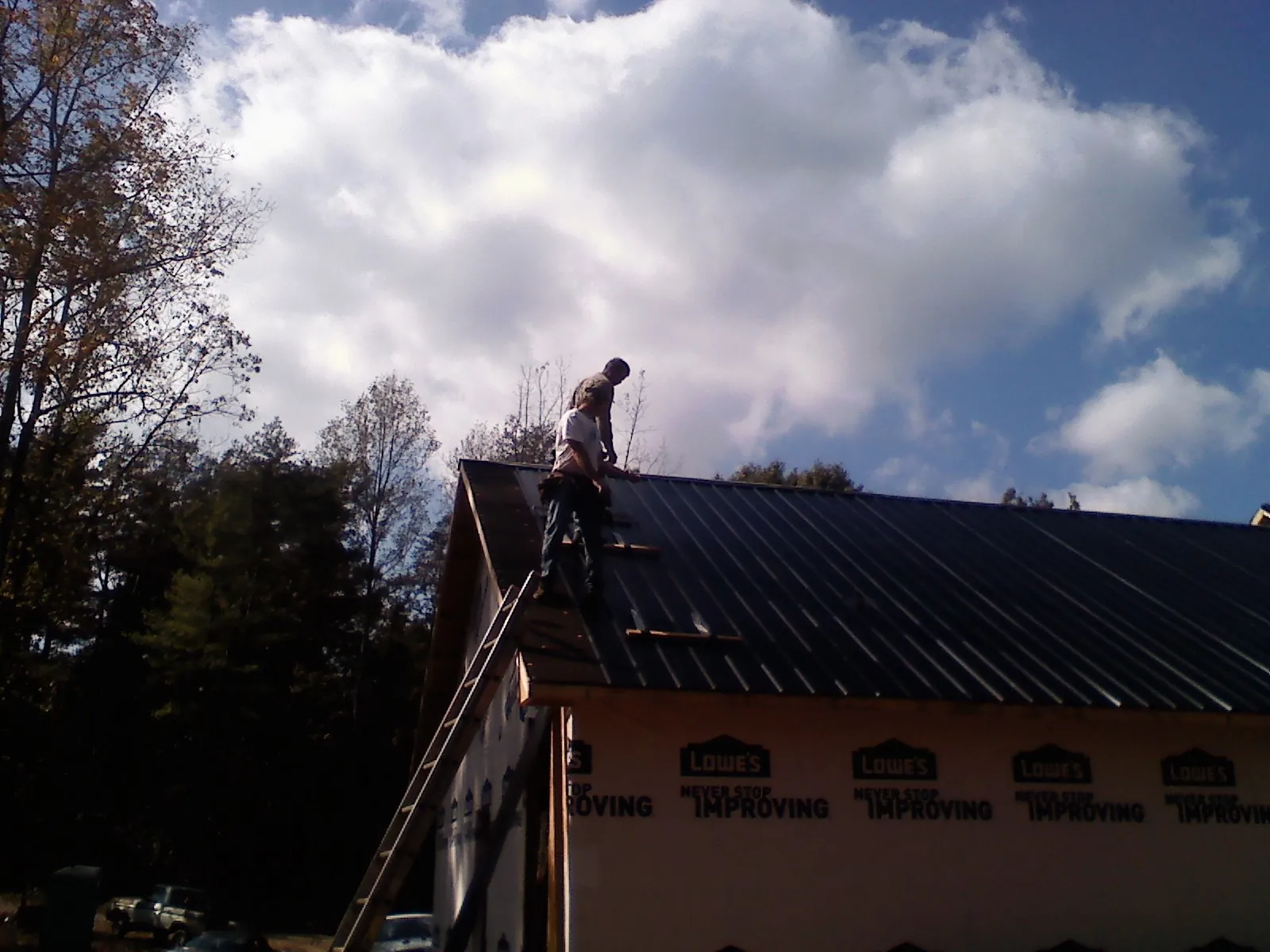 Roofer fastening dark metal panels high against a cloudy sky, from a Roof Inspection job in La Habra