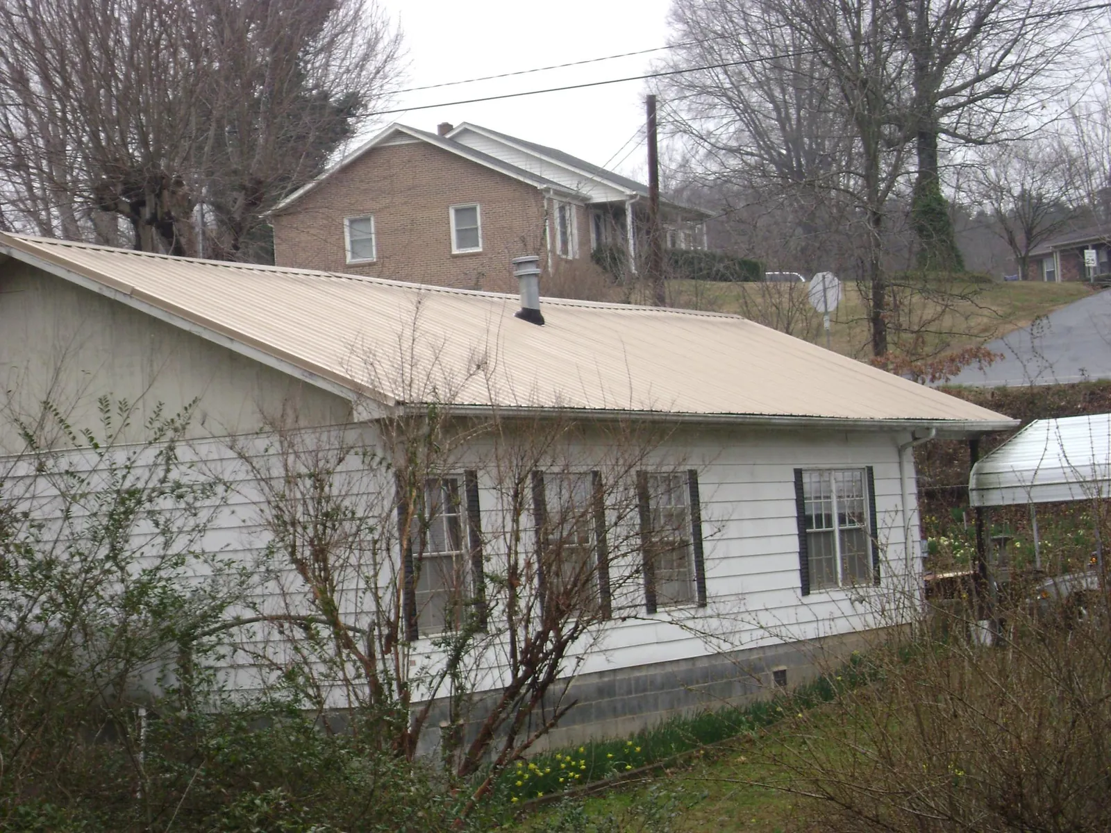 Tan metal roof on a white sided house set into a hillside — Commercial Roofing by Roofing Brothers in La Habra